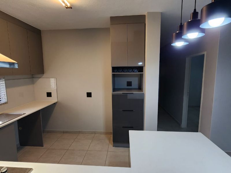 Modern kitchen featuring sleek grey cabinetry, tiled flooring, integrated extractor fan, and a functional layout with ample counter space and pendant lighting.