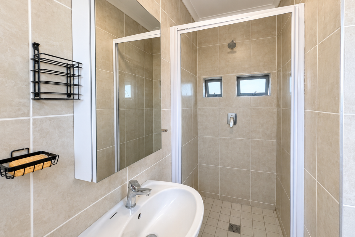 A clean, functional bathroom featuring a tiled shower enclosure, a modern vanity basin with mixer tap, and a mirrored medicine cabinet.