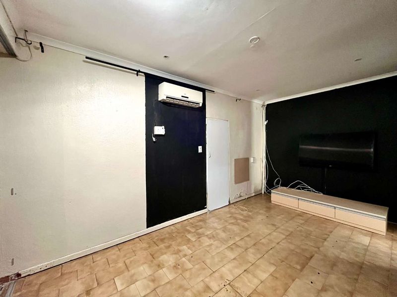 Living area featuring tiled flooring and a wall-mounted air conditioning unit, requiring cosmetic updates and repairs to wall finishes and flooring.