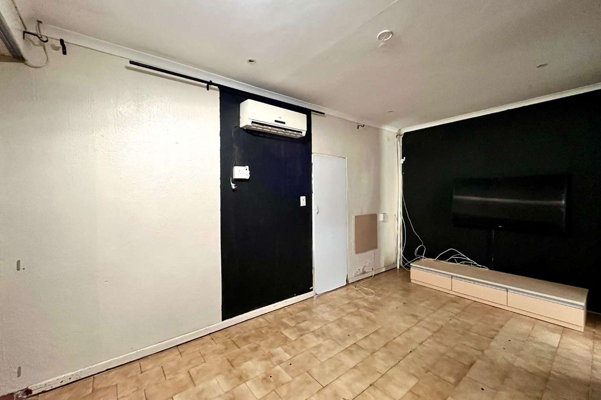 Living area featuring tiled flooring and a wall-mounted air conditioning unit, requiring cosmetic updates and repairs to wall finishes and flooring.