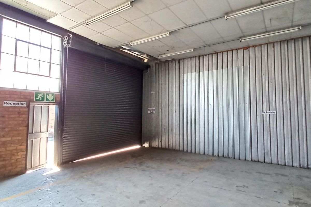 Spacious industrial warehouse unit featuring a large roller shutter door, exposed brick walls, steel cladding, and high-clearance ceilings with fluorescent lighting.