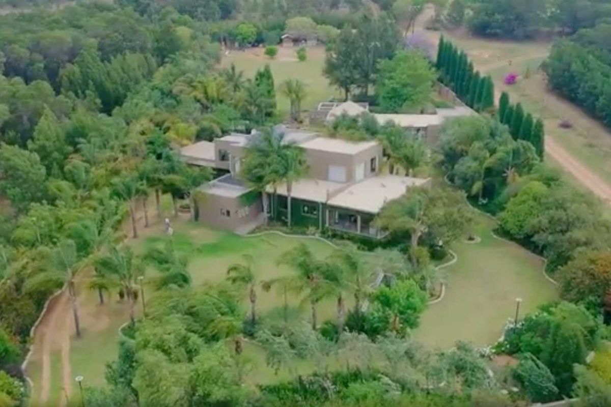 Aerial view of a spacious small holding property featuring a multi-level residence surrounded by extensive landscaped gardens, mature trees, and a private driveway.