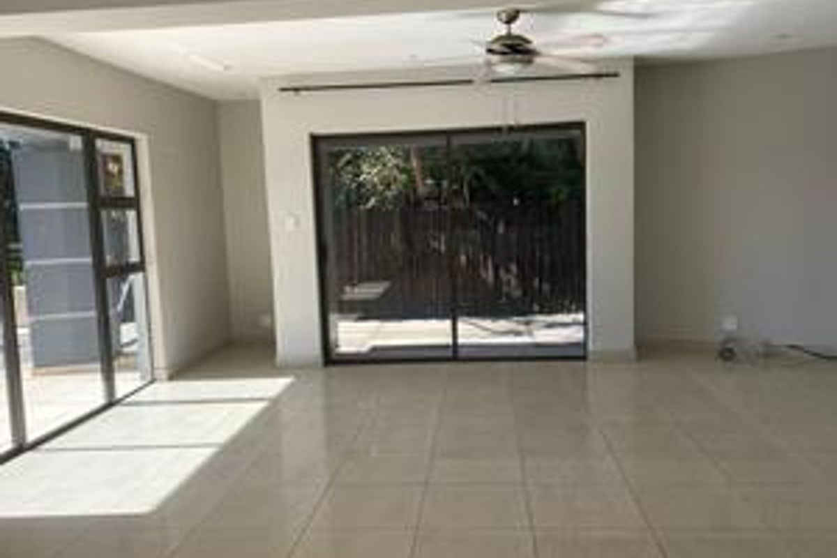Spacious, light-filled living area featuring neutral tiled flooring, a modern ceiling fan, and large sliding glass doors providing access to the outdoor space.