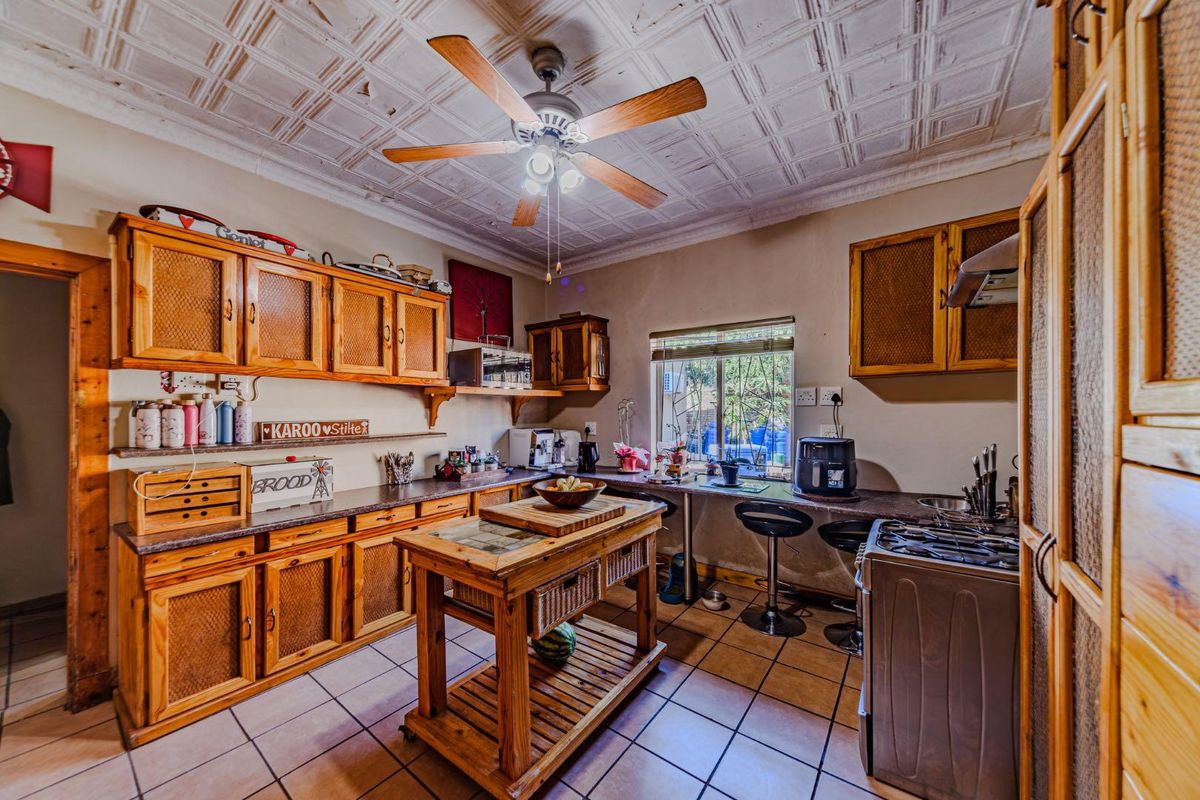 A rustic kitchen featuring wooden cabinetry, tiled flooring, a pressed metal ceiling, and a central island, offering a functional space with potential for modernization.