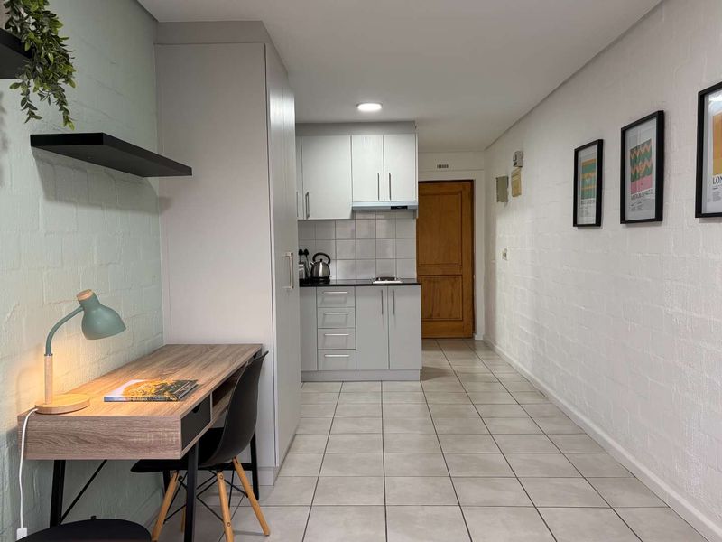 An open-plan apartment layout featuring a compact kitchen with modern cabinetry and tiled flooring, seamlessly flowing into a functional living or workspace area.