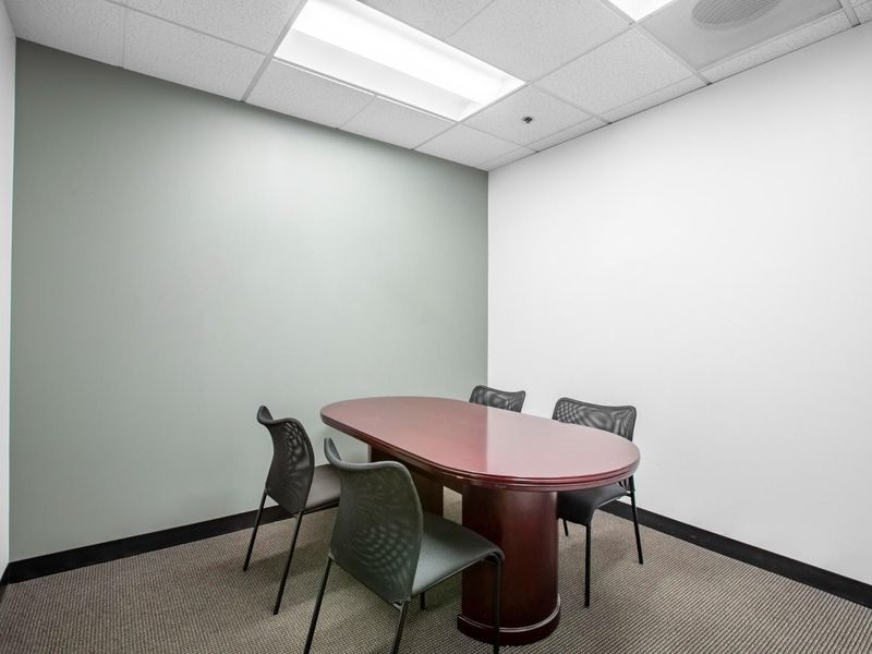 A professional office meeting room featuring a suspended ceiling, recessed lighting, and carpeted flooring.