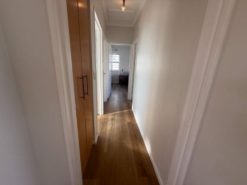 A clean, well-maintained hallway featuring timber flooring and a built-in storage cupboard, providing access to adjacent rooms.