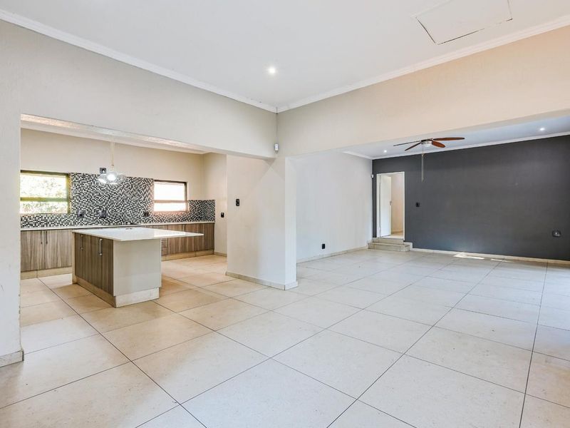 Spacious open-plan living and kitchen area featuring tiled flooring, a central kitchen island, and a modern mosaic backsplash.