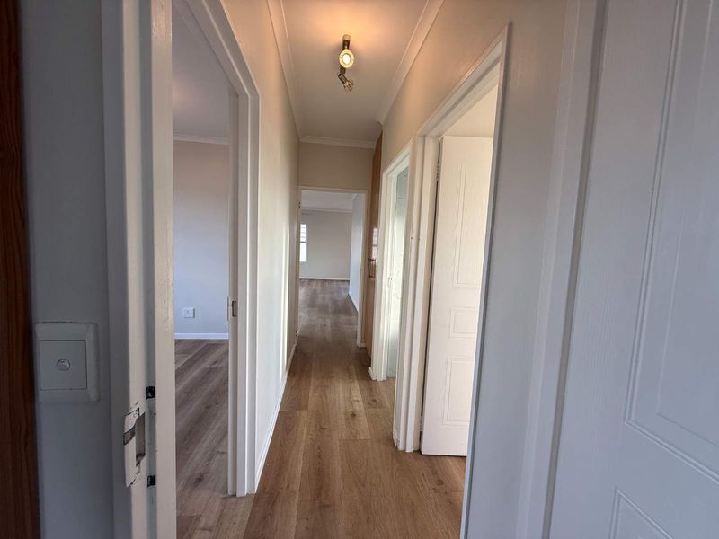 A clean, well-maintained hallway featuring modern laminate flooring and neutral wall finishes, providing access to multiple rooms within the home.