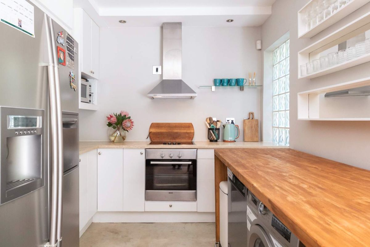 Modern kitchen featuring white cabinetry, stainless steel appliances, a wooden countertop, and a unique glass block window for natural light.