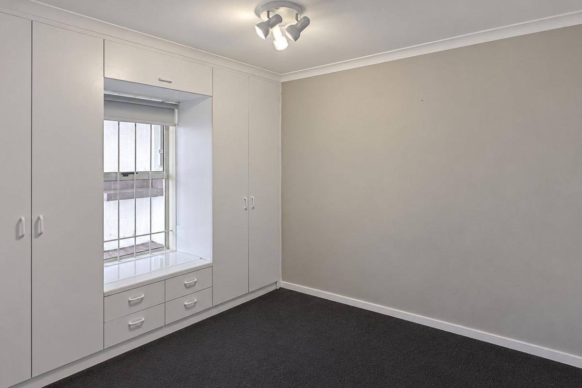 A clean, empty bedroom featuring neutral walls, dark carpeting, and extensive built-in cabinetry with an integrated window seat and storage drawers.