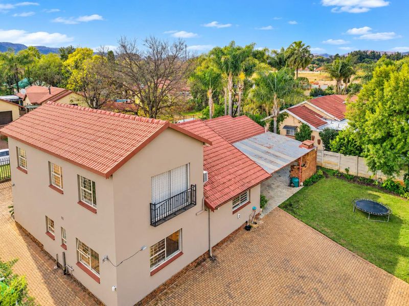Aerial view of a two-story residential property featuring a terracotta tile roof, paved driveway, and a covered patio area set within a landscaped garden.