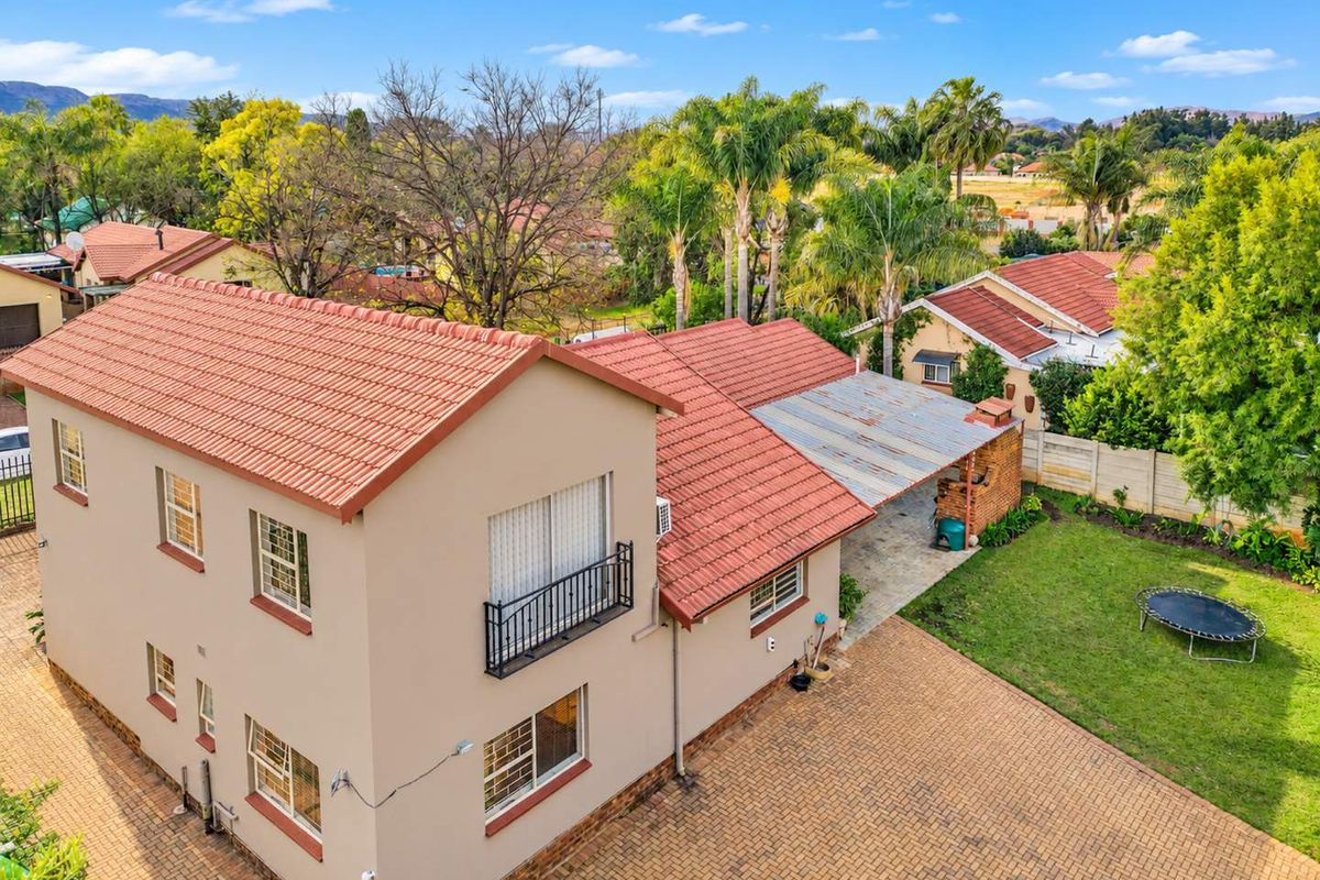 Aerial view of a two-story residential property featuring a terracotta tile roof, paved driveway, and a covered patio area set within a landscaped garden.