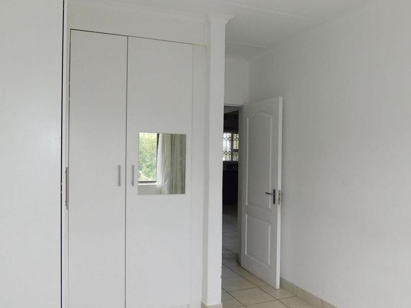A clean, empty bedroom featuring built-in cupboards and neutral tiled flooring, offering a blank canvas for personalization.