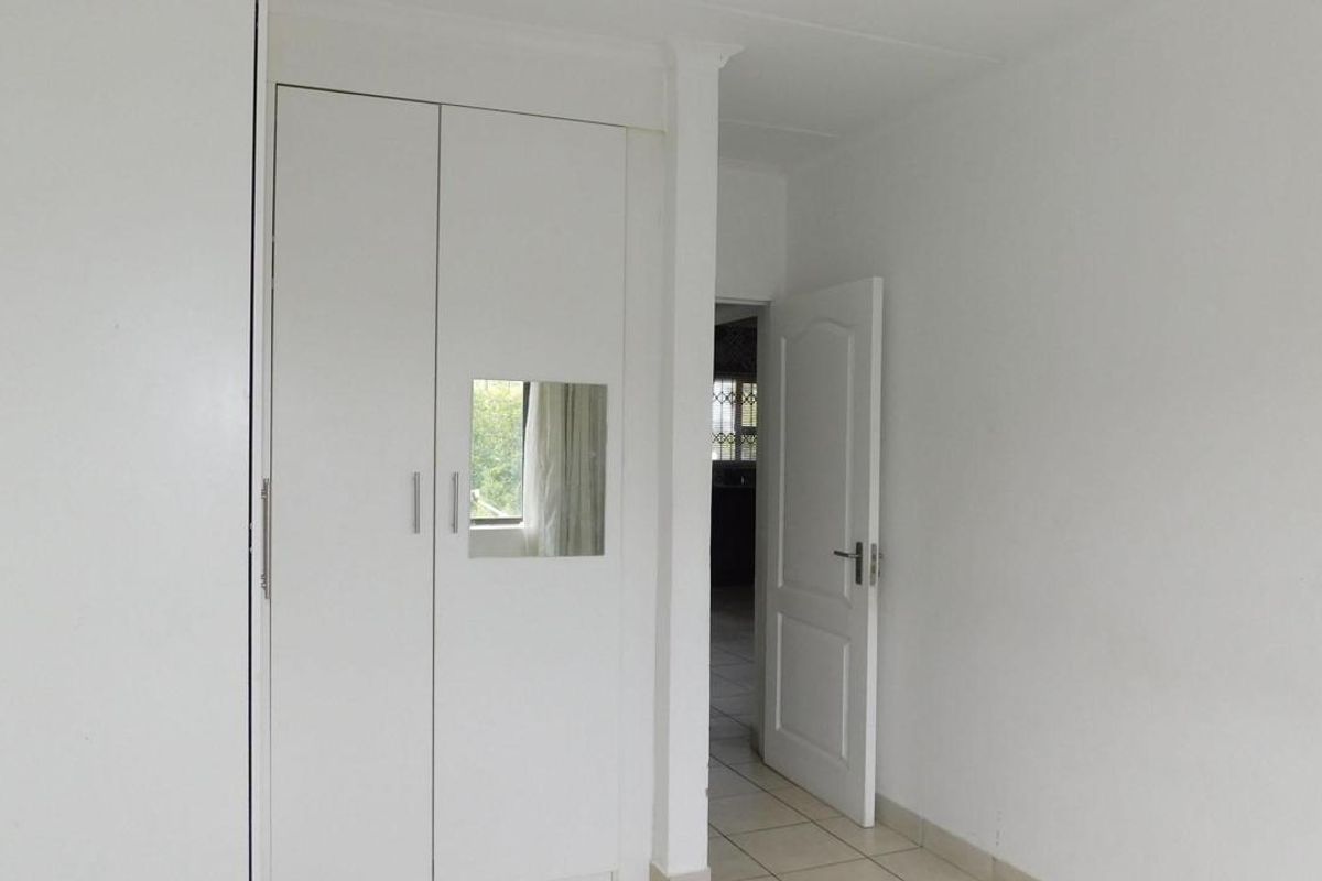 A clean, empty bedroom featuring built-in cupboards and neutral tiled flooring, offering a blank canvas for personalization.