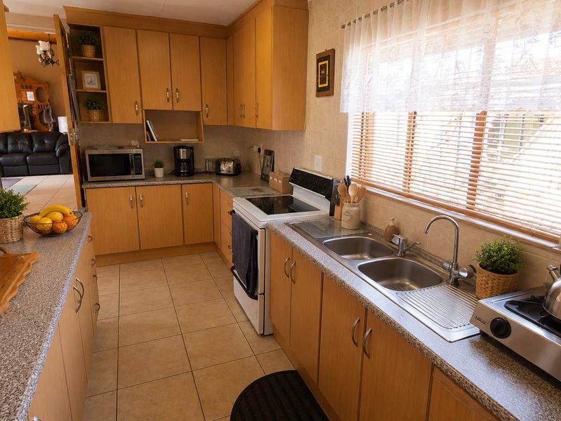 A functional kitchen featuring light wood-tone cabinetry, granite-look laminate countertops, a double stainless steel sink, and tiled flooring.