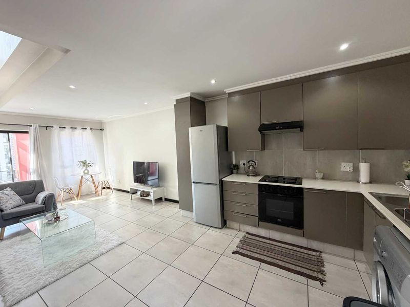 Modern open-plan living area featuring a sleek kitchen with built-in cabinetry, integrated appliances, and tiled flooring, seamlessly flowing into the lounge space.