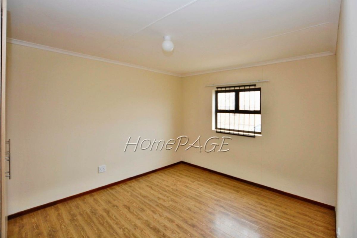 A clean, empty bedroom featuring wood-look laminate flooring, neutral walls, and a window fitted with security bars.