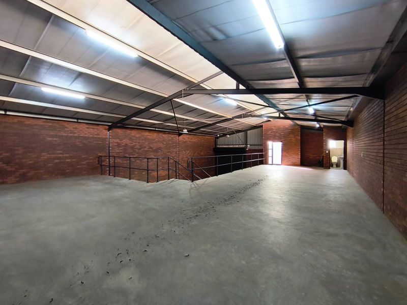 Spacious industrial mezzanine area featuring exposed brick walls, concrete flooring, and steel roof trusses, suitable for storage or workshop use.