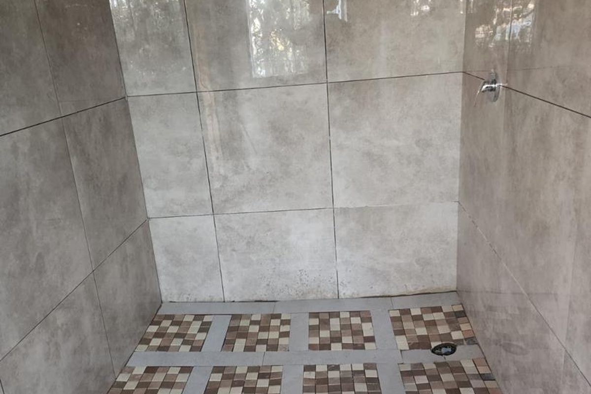 A modern walk-in shower featuring large format grey wall tiles, a mosaic tiled shower floor, and a contemporary rain shower head.