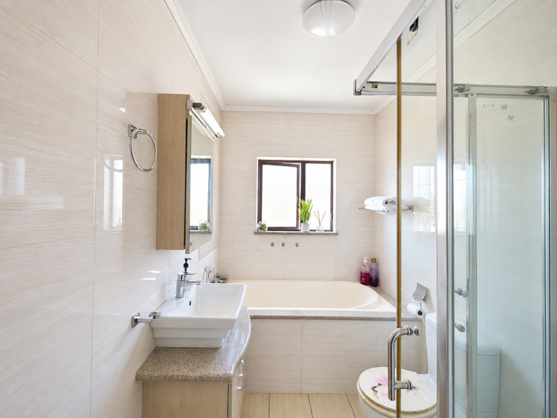 A well-maintained bathroom featuring a built-in vanity, a bathtub, a separate glass-enclosed shower, and neutral wall tiling.