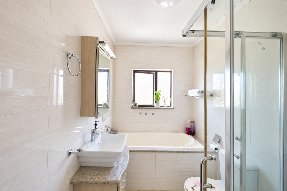 A well-maintained bathroom featuring a built-in vanity, a bathtub, a separate glass-enclosed shower, and neutral wall tiling.