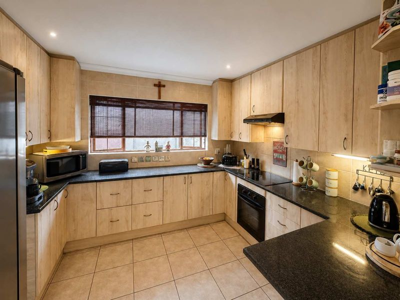 A functional U-shaped kitchen featuring light wood-grain cabinetry, dark granite countertops, ceramic tile flooring, and integrated appliances including an oven and extractor fan.