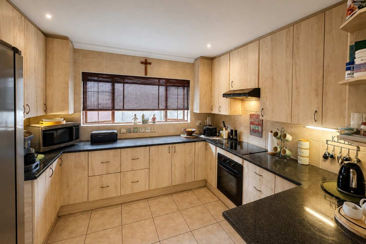A functional U-shaped kitchen featuring light wood-grain cabinetry, dark granite countertops, ceramic tile flooring, and integrated appliances including an oven and extractor fan.
