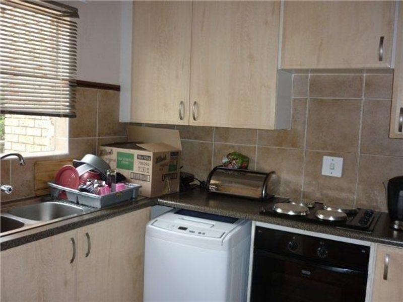 Compact kitchen featuring laminate cabinetry, tiled backsplash, built-in oven, electric hob, and a double bowl stainless steel sink.