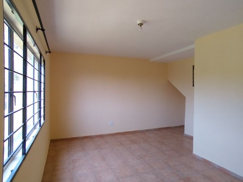 An empty, neutrally painted living area featuring tiled flooring and large windows with security bars, offering a blank canvas for interior design.