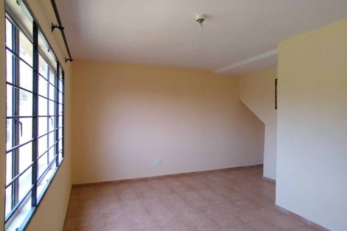 An empty, neutrally painted living area featuring tiled flooring and large windows with security bars, offering a blank canvas for interior design.