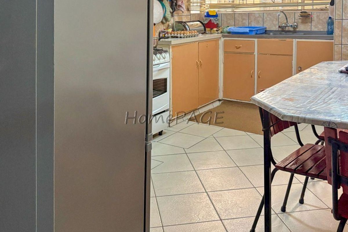 A dated kitchen featuring original cabinetry, tiled flooring, a stainless steel sink, and a freestanding stove, offering potential for a modern renovation.