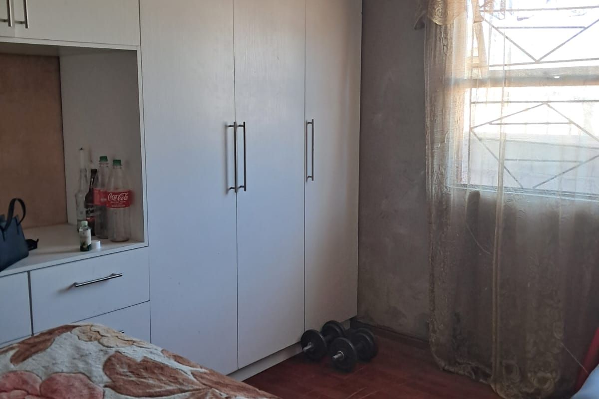 Bedroom featuring built-in cupboards, laminate flooring, and a window with security bars. The room requires wall and ceiling finishing to improve its overall condition.