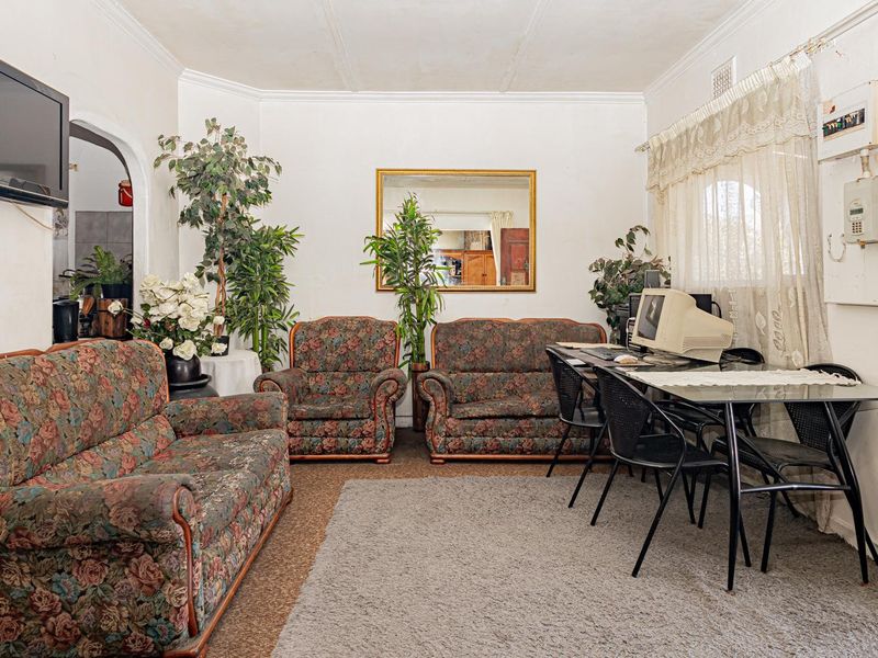 A living room featuring an arched entryway, coved ceilings, and an exposed electrical distribution board, showing signs of wear and dated finishes.