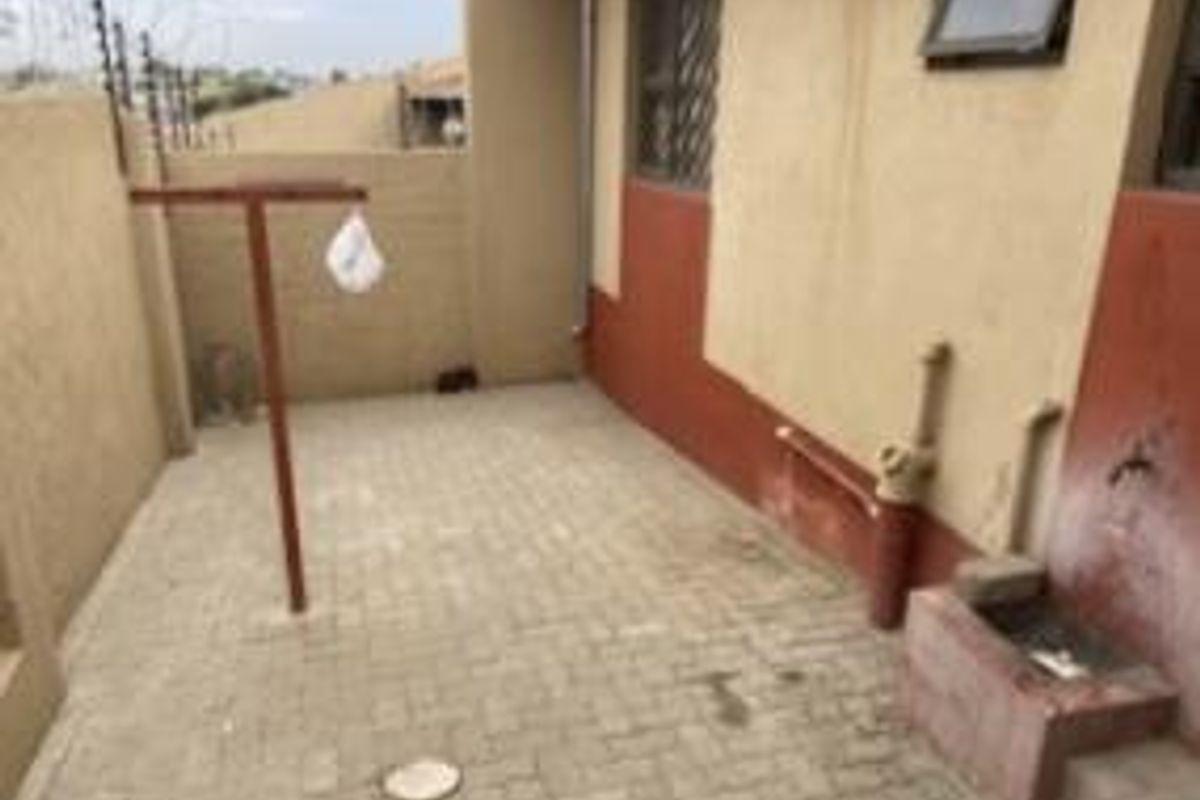 A functional outdoor utility area featuring paved flooring, a fixed washing line, and exterior plumbing connections against a rendered wall.