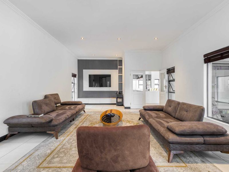Spacious living room featuring modern tiled flooring, recessed downlighting, and a contemporary feature wall with a built-in media unit.