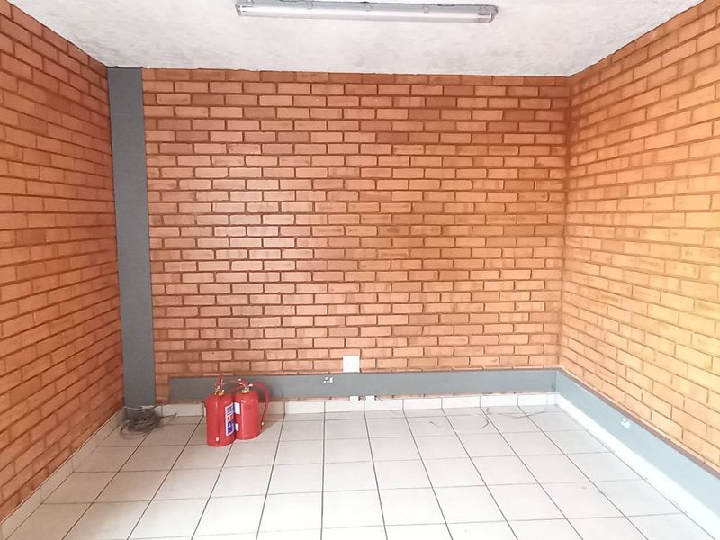 A functional industrial office space featuring exposed brick walls, tiled flooring, and overhead fluorescent lighting, suitable for a variety of commercial uses.