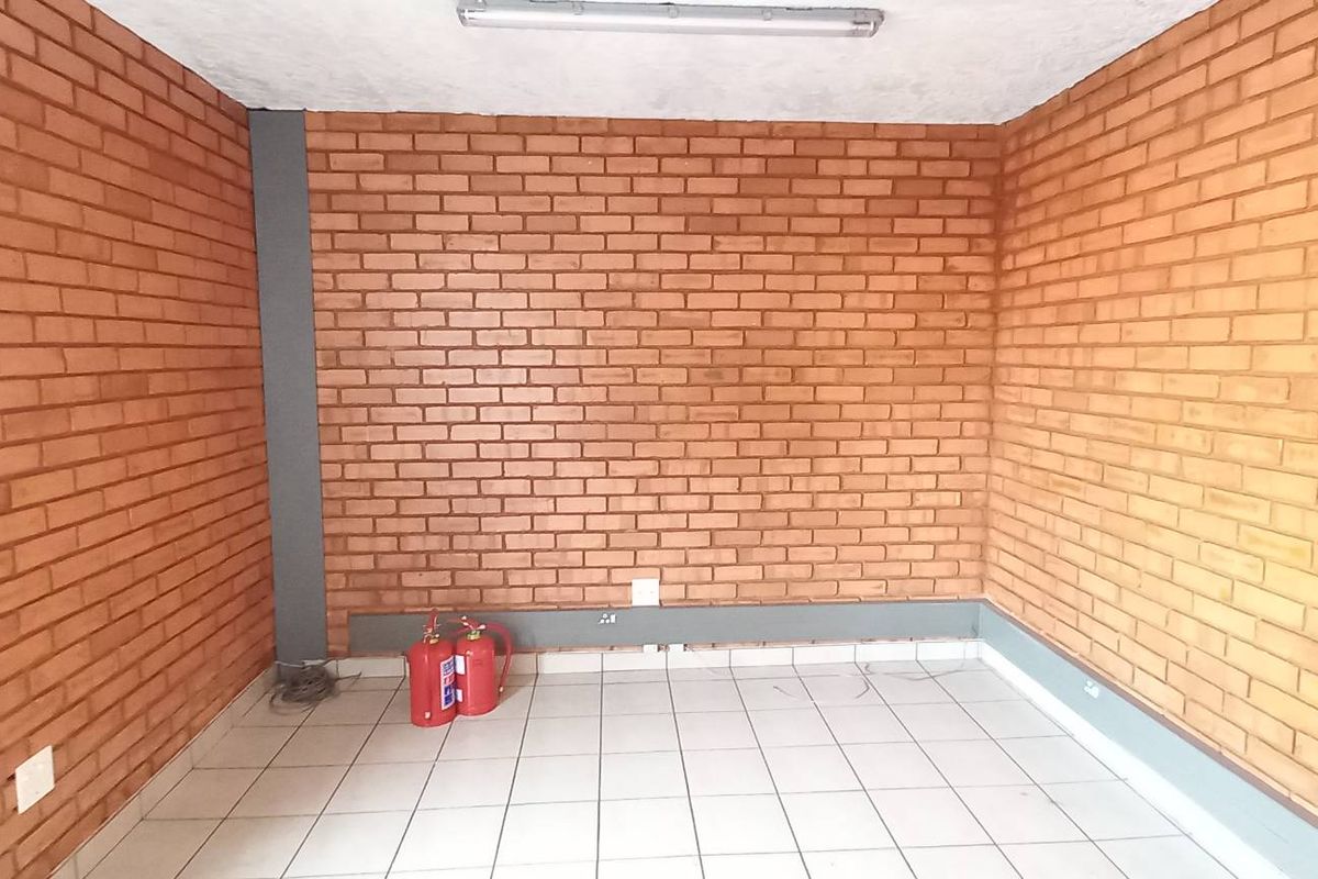 A functional industrial office space featuring exposed brick walls, tiled flooring, and overhead fluorescent lighting, suitable for a variety of commercial uses.