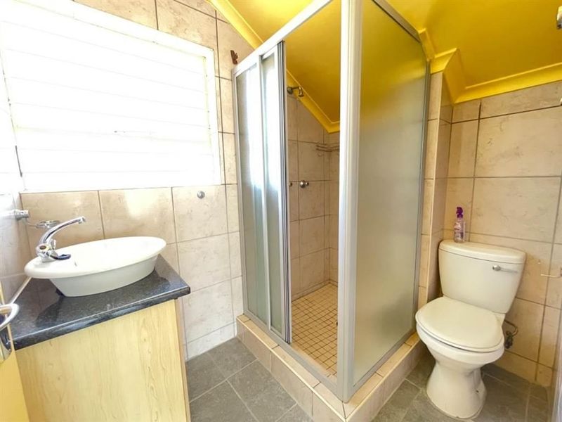 A functional bathroom featuring a shower enclosure, vanity with vessel sink, and toilet, finished with neutral wall tiles.