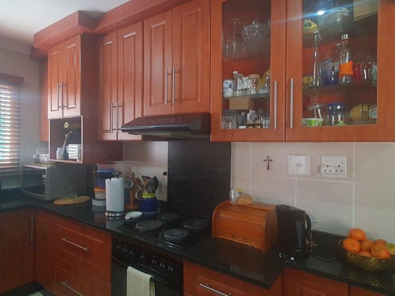 A functional kitchen featuring warm-toned wooden cabinetry, granite countertops, a built-in electric hob, and an extractor fan with glass-fronted display units.
