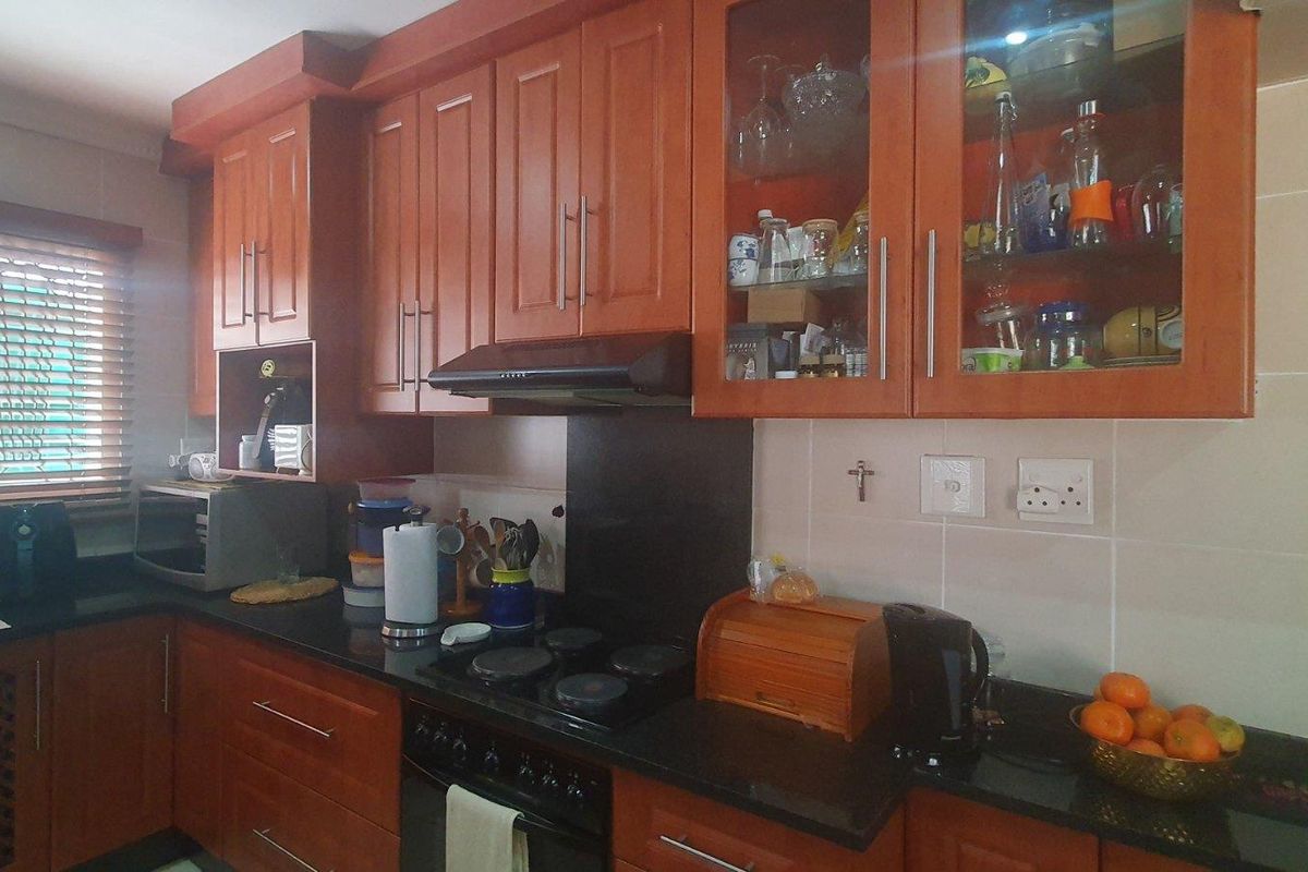 A functional kitchen featuring warm-toned wooden cabinetry, granite countertops, a built-in electric hob, and an extractor fan with glass-fronted display units.
