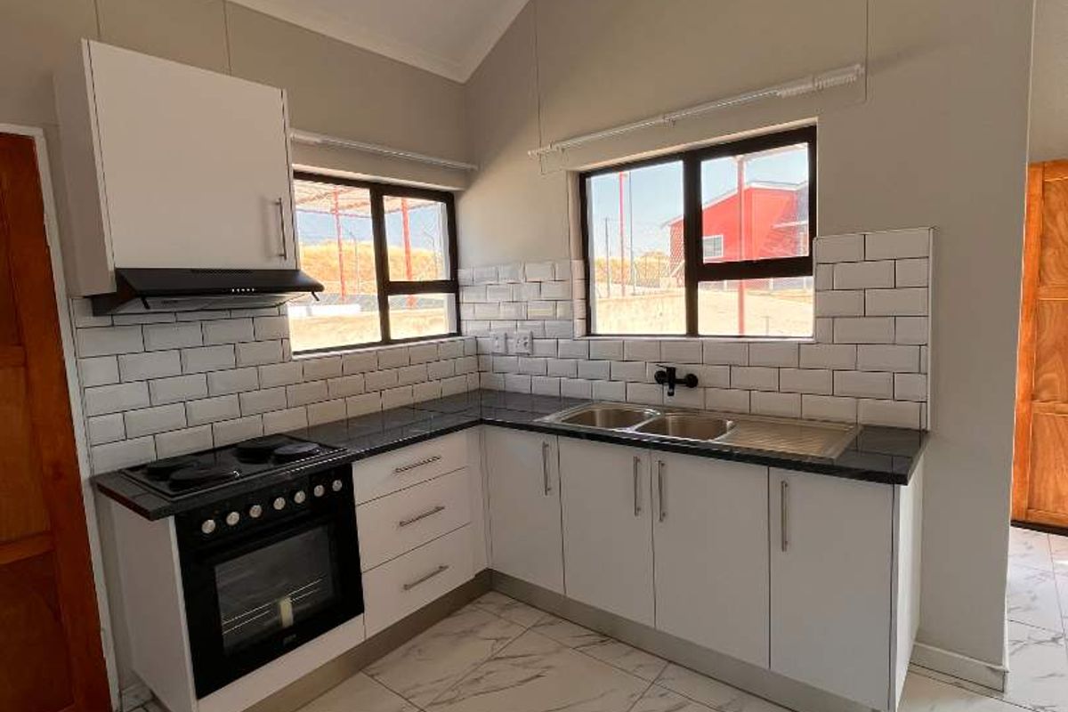 Modern kitchen featuring white cabinetry, dark countertops, subway tile backsplash, built-in oven with hob, and marble-look floor tiles under a vaulted ceiling.