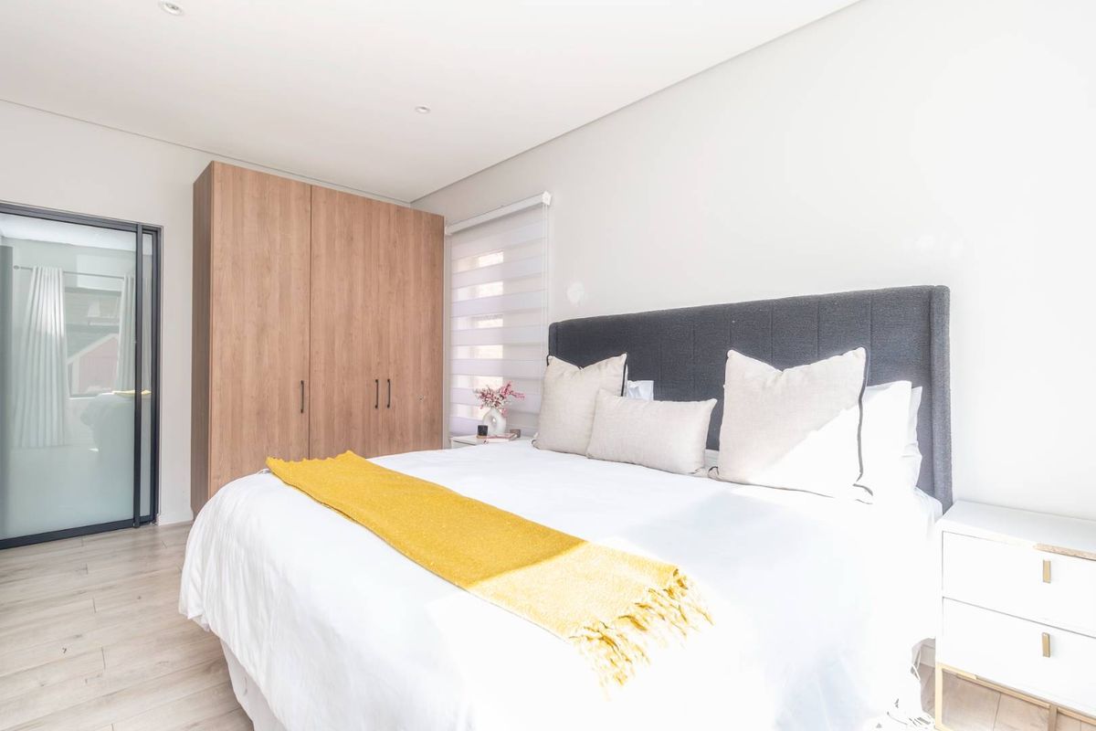 A bright and modern bedroom featuring light laminate flooring, a built-in wooden wardrobe, and recessed ceiling lighting.