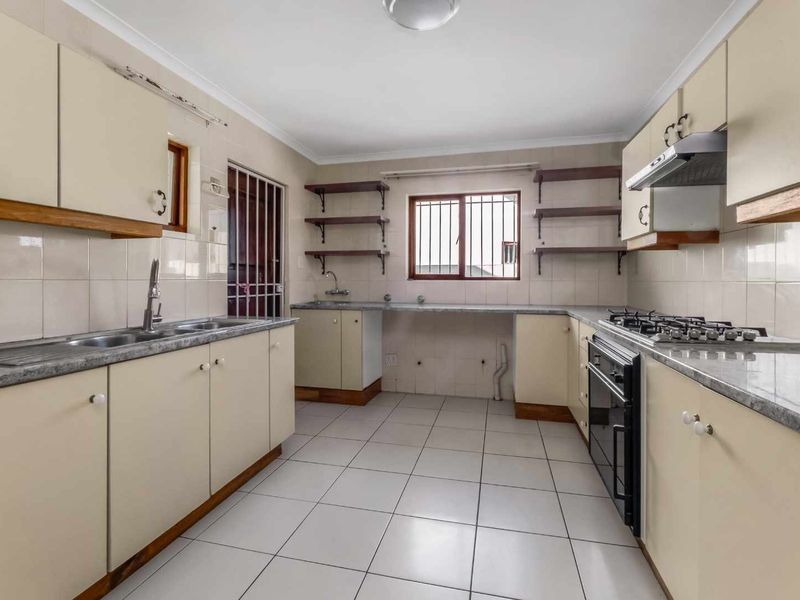 A functional kitchen featuring built-in cabinetry, laminate countertops, a gas hob, and an integrated oven, with tiled flooring and security features on the windows.