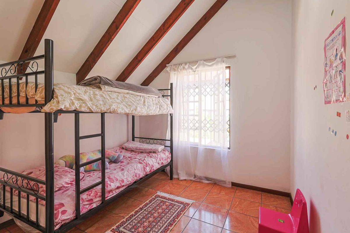 A bedroom featuring exposed timber rafters, tiled flooring, and a window fitted with a security gate.