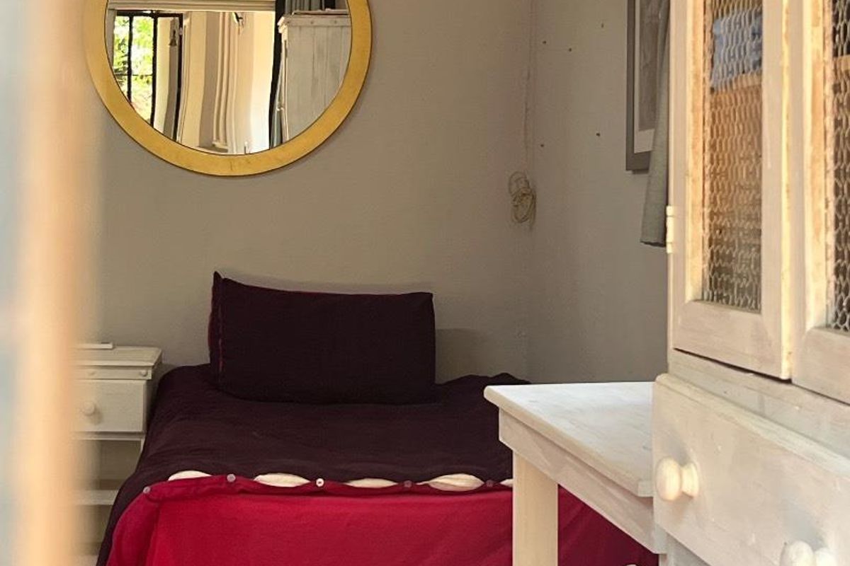 A cozy bedroom featuring terracotta floor tiles and a neutral wall finish, viewed through a doorway.