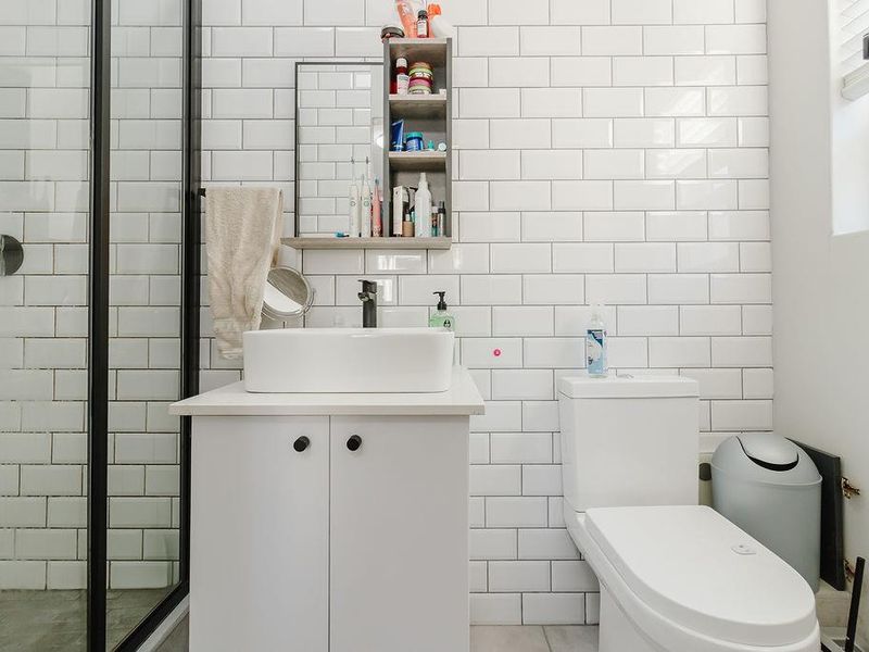 Modern bathroom featuring white subway tile walls, a sleek vessel sink vanity, a toilet, and a walk-in shower with a black-framed glass enclosure.