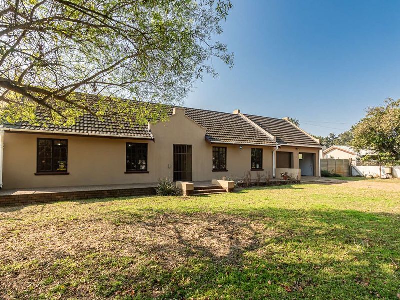 Rear view of the property featuring a tiled roof, brick patio, and attached garage, set against a spacious garden area.