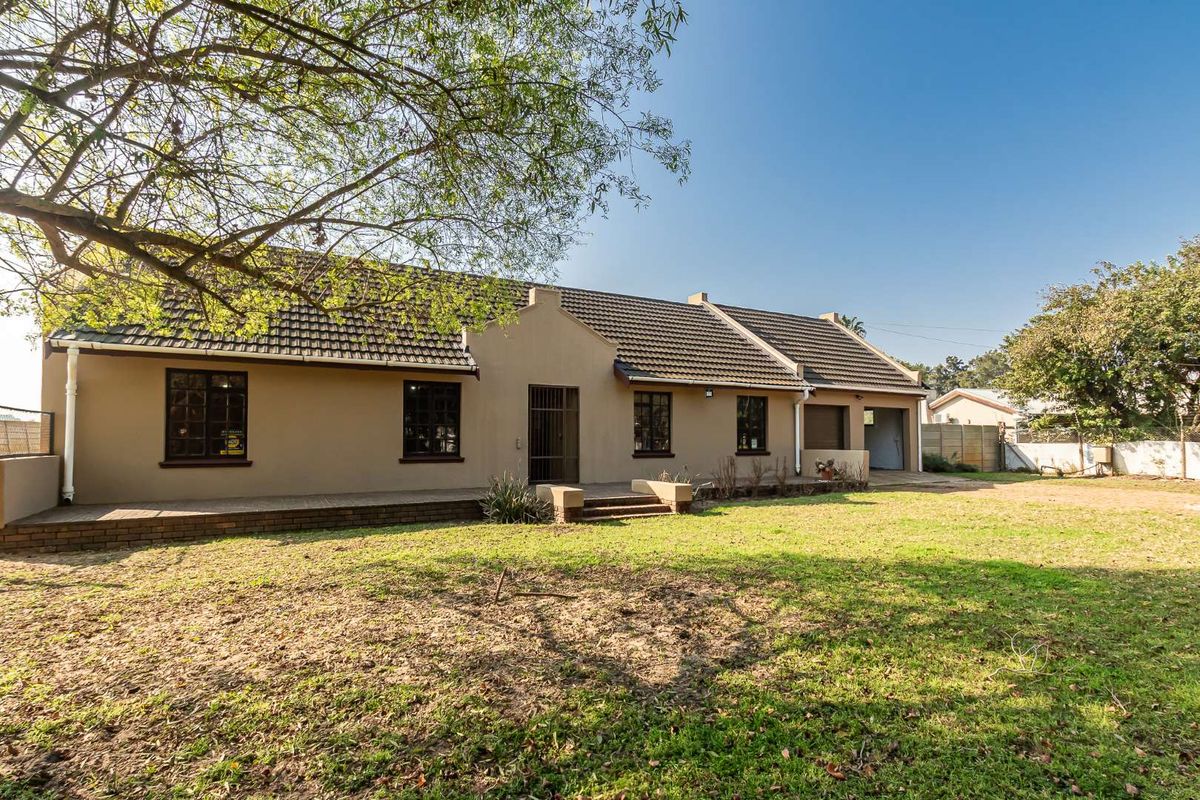 Rear view of the property featuring a tiled roof, brick patio, and attached garage, set against a spacious garden area.