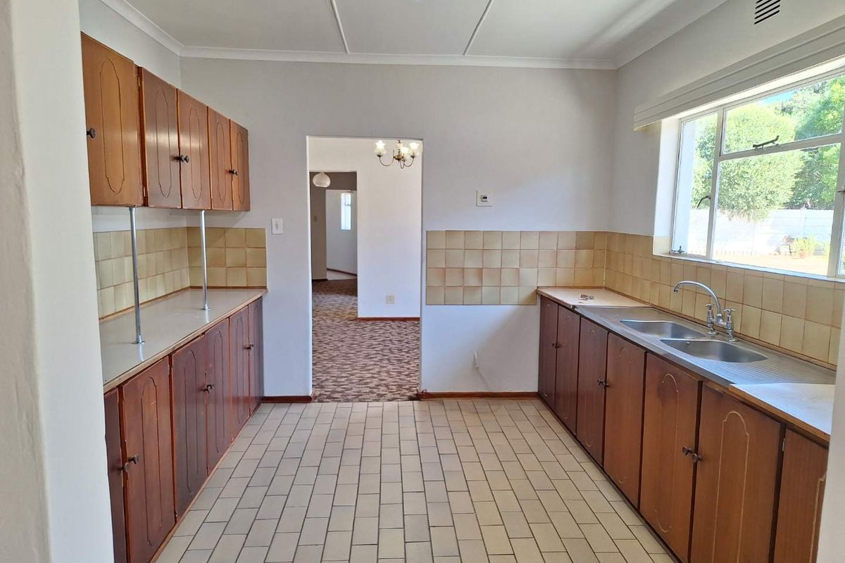A functional kitchen featuring traditional wooden cabinetry, tiled flooring, and a double-basin stainless steel sink with a view of the exterior.